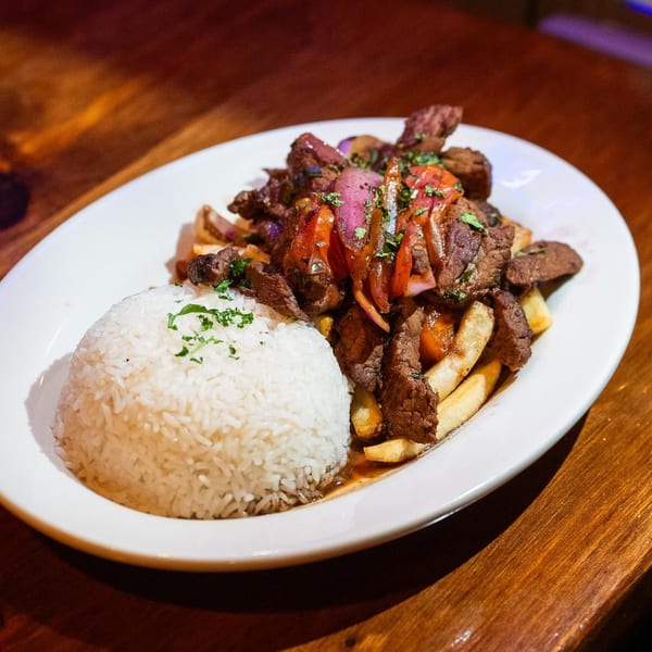 A plate of Lomo Saltado with steak, fries, onions, tomatoes, and a side of white rice.