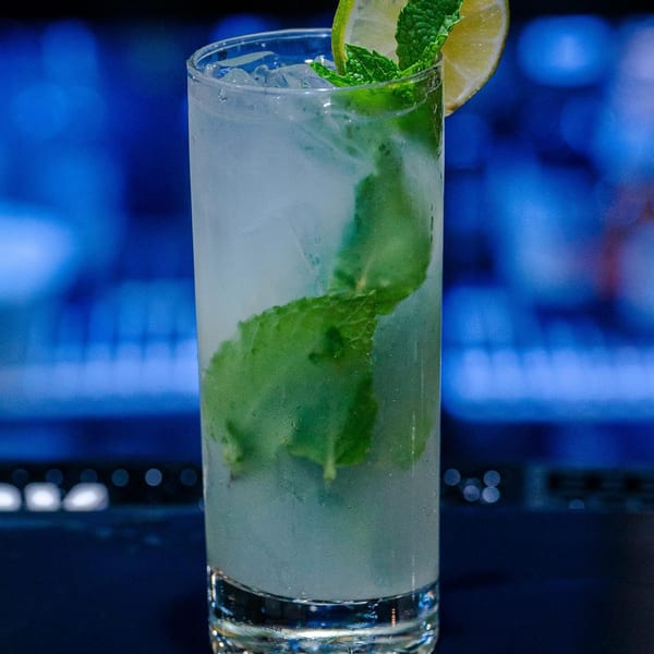 A refreshing mojito cocktail with mint leaves and a lime wedge, against a blurred blue background.
