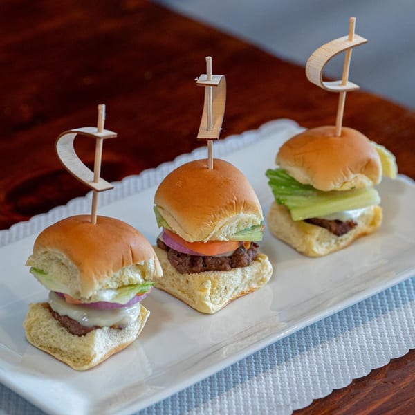 Three Catharsis Bar & Grill sliders with cheese, lettuce, tomato, and onion on a white platter.