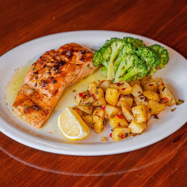 Grilled salmon with a lemon wedge, roasted potatoes, and steamed broccoli on a white plate.
