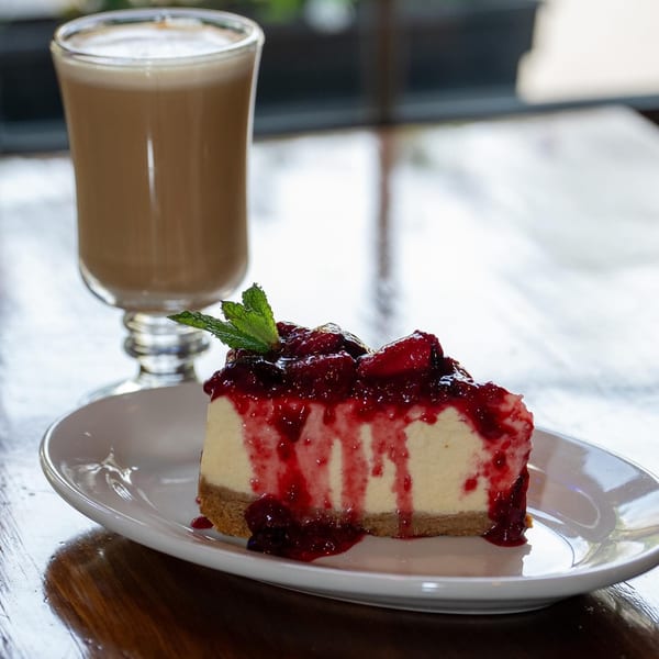 A slice of cheesecake with berry topping and mint, next to a glass of iced coffee.